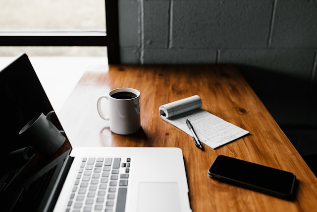 A MacBook Pro placed on a table with a cup, notebook, and phone on the side